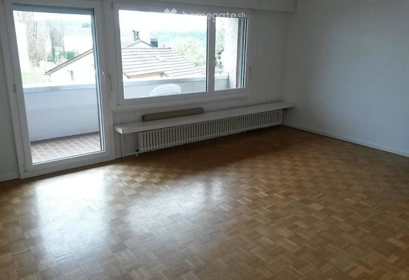 Empty room with wooden flooring, large windows, and a balcony access. No furniture or equipment present.
