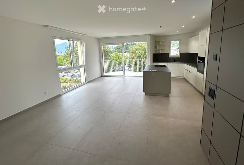 Empty kitchen with tiled floor, white walls, large windows, and a central island. No furniture or appliances are present.