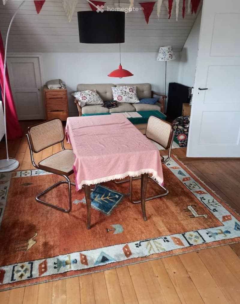 A cozy living room with a sofa, a small table with chairs, a colorful rug, and a floor lamp.