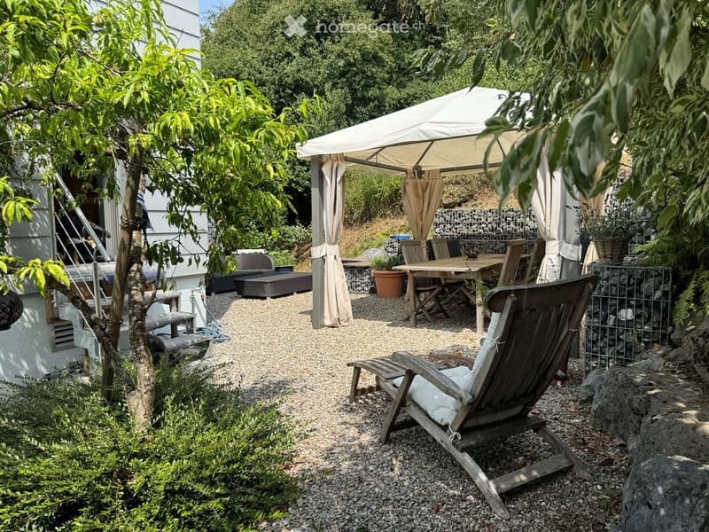 A well-maintained garden area with a wooden deck, outdoor furniture, a large umbrella, and lush greenery.