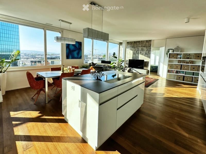 Modern open-plan kitchen and dining area with white cabinetry, a central island, pendant lights, a dining table with red chairs, and a view of the cityscape through large windows.
