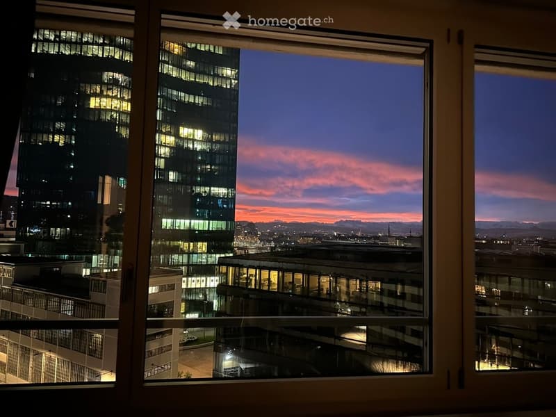 View from a balcony showing cityscape with modern buildings and sunset sky.