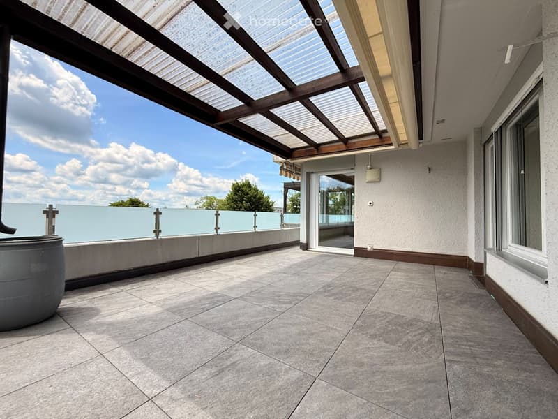 Balcony with tiled floor, modern glass railing, and a covered section with wooden beams and translucent roof panels.