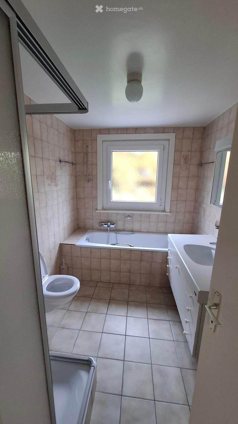 Bathroom with tiled walls and floor, featuring a toilet, bathtub, sink, and shower stall. A window provides natural light.