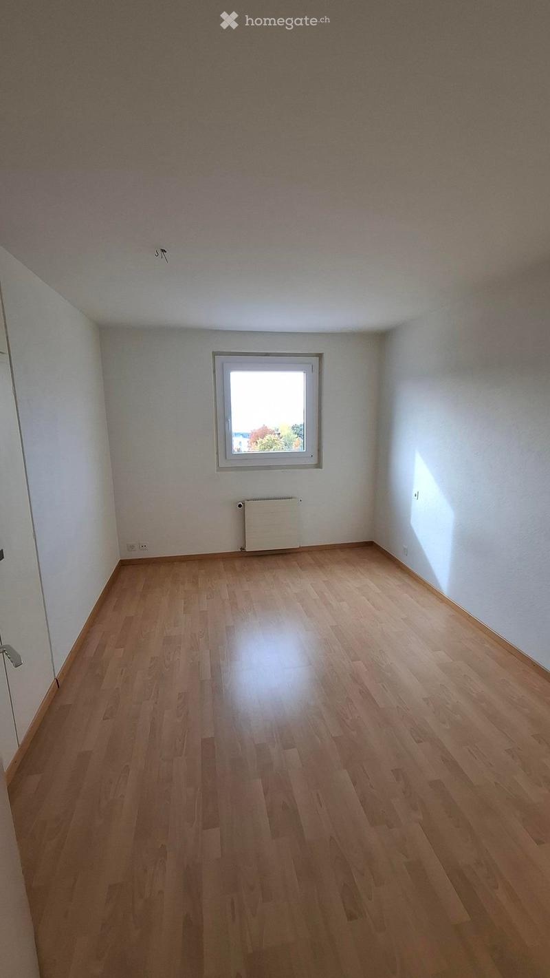Empty room with wooden flooring, white walls, and a single window with a radiator below it.