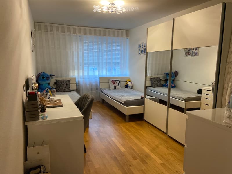 Modern bedroom with two single beds, a desk, chair, mirror, wardrobe, and decorative items.
