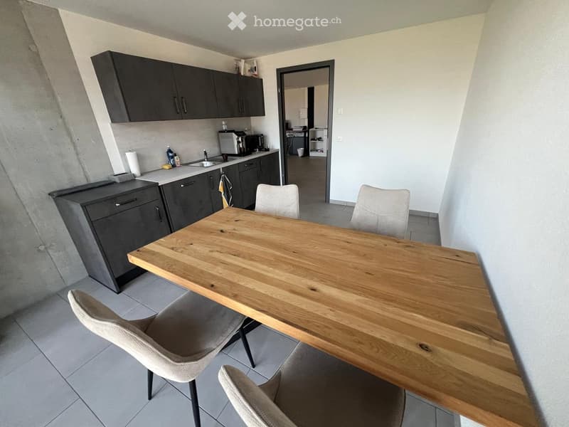 Modern kitchen with dark grey cabinets, a wooden dining table, four chairs, and a sink area with a microwave and oven.