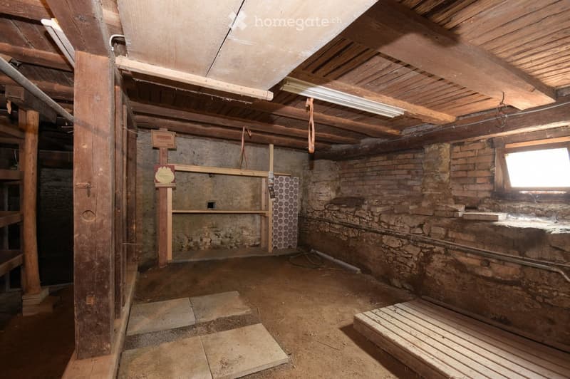 Empty room with exposed wooden beams, stone walls, and a small window. The floor is unfinished, and there are no furnishings or equipment visible.