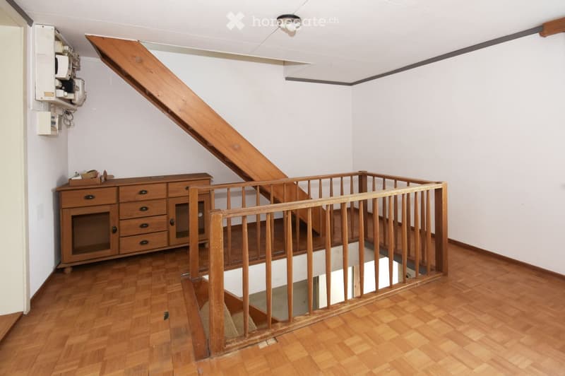 Wooden staircase with a wooden railing, wooden floor, white walls, and a wooden cabinet with drawers and doors on the left side.