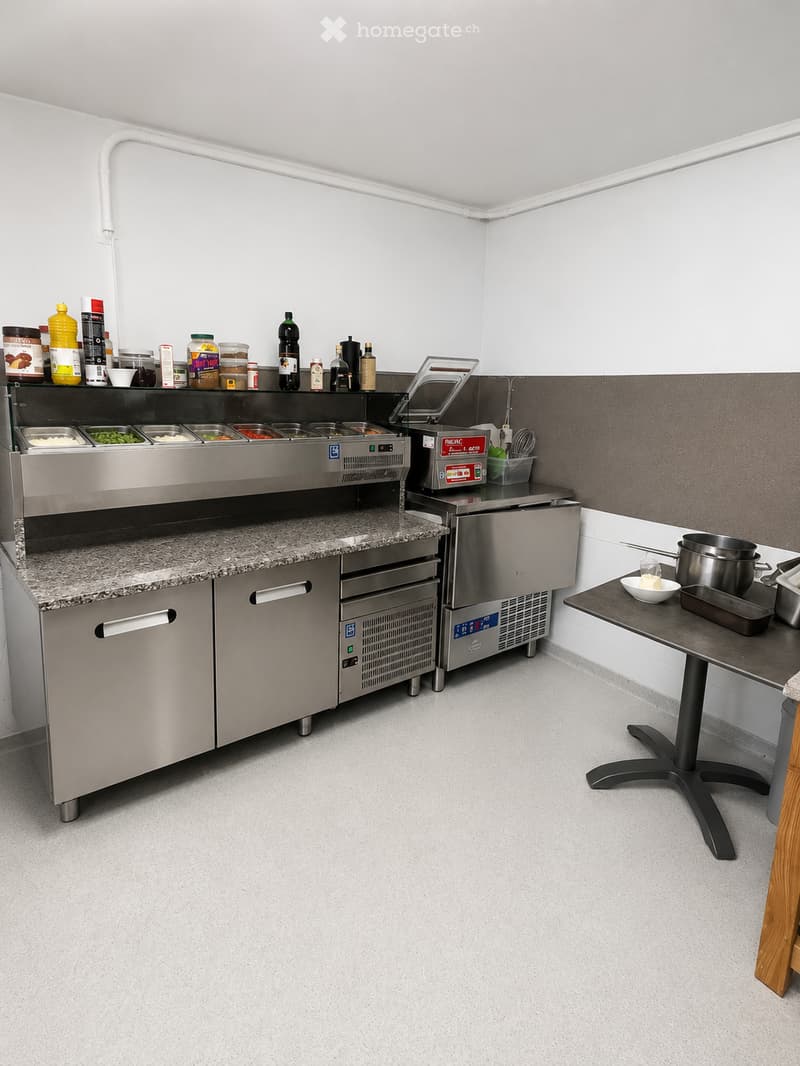 Commercial kitchen with stainless steel appliances, granite countertop, and various food containers and utensils.