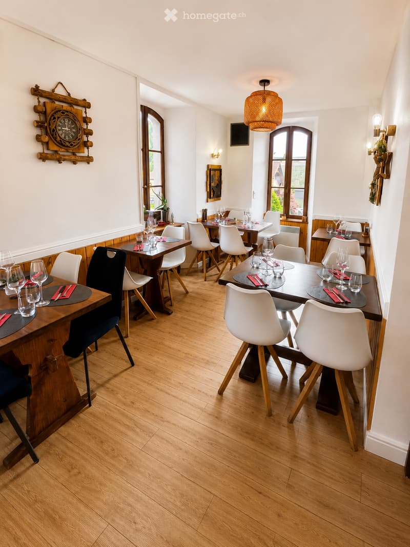 Dining area with wooden tables, white chairs, wine glasses, and a clock on the wall.