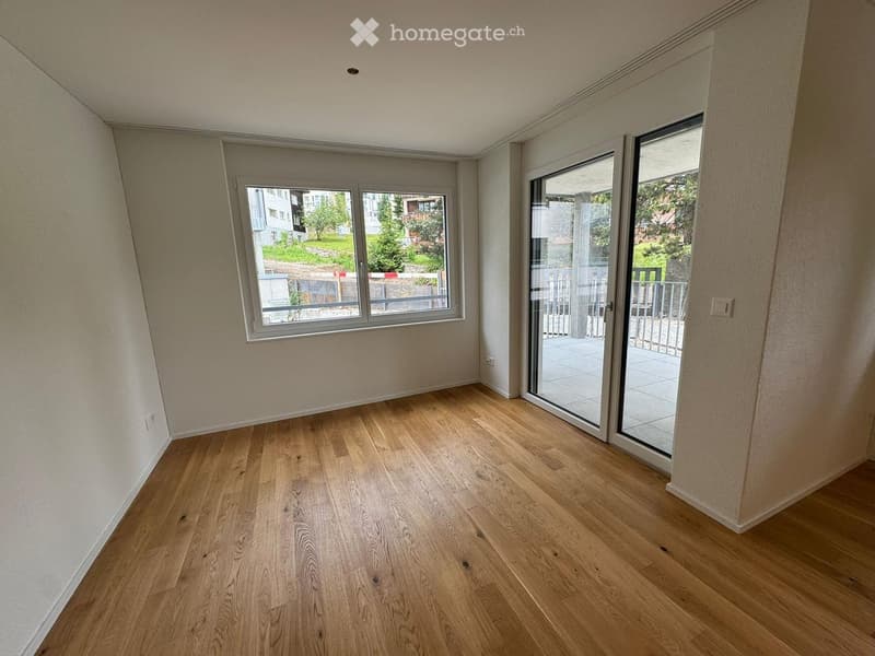 Empty room with wooden flooring, large windows, and sliding glass doors leading to a balcony.