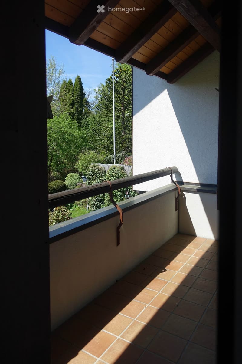Balcony with wooden railing, tiled floor, view of trees and plants