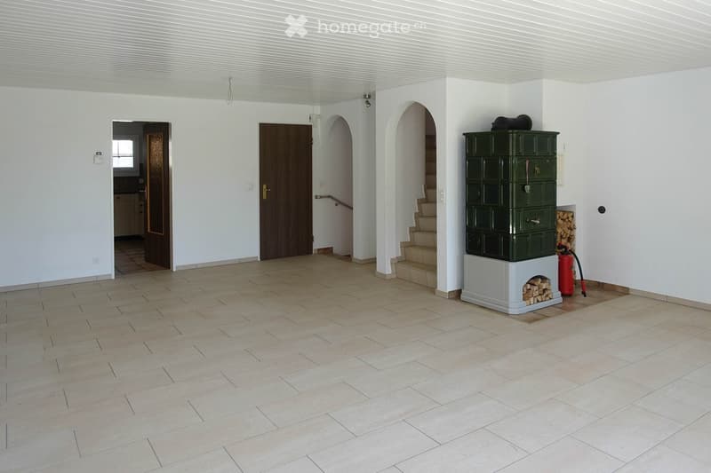 Empty room with white walls, tiled floor, two doors, staircase, fireplace, and a fire extinguisher.