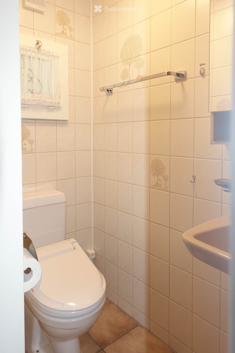 Bathroom with white tiles, white toilet, white sink, towel rack, small window with curtain