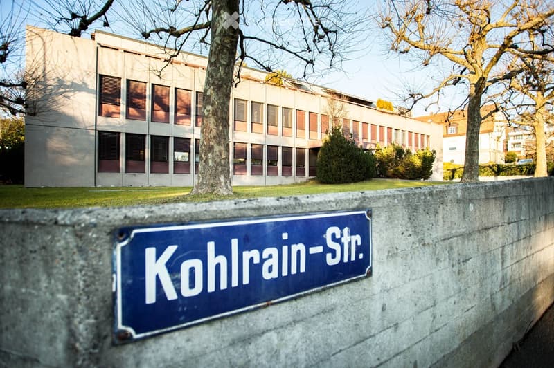 Modern multi-story building with large windows and a sign reading "Kohlrain-Str." in front of a concrete wall.