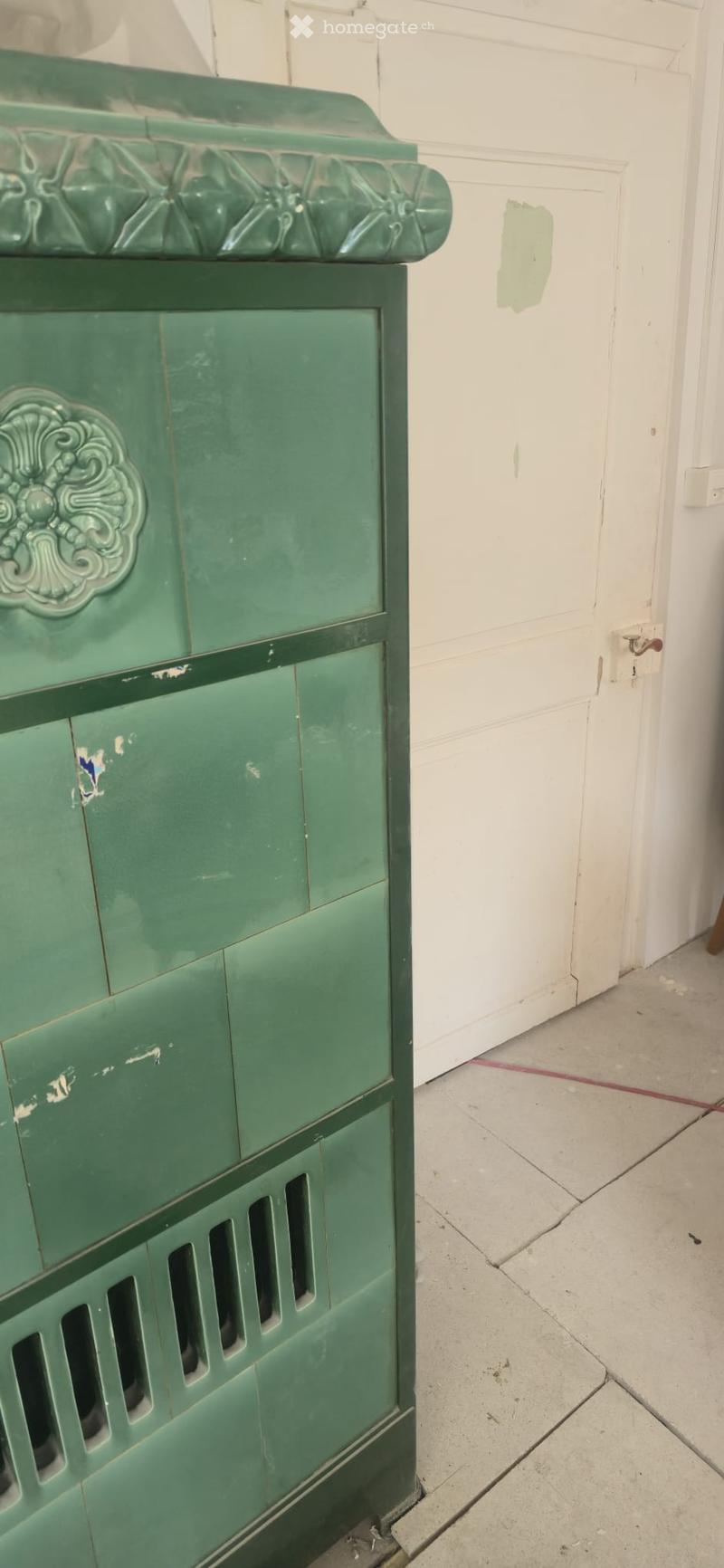 An unfurnished room with a green cabinet featuring ornate carvings and a white door in the background.