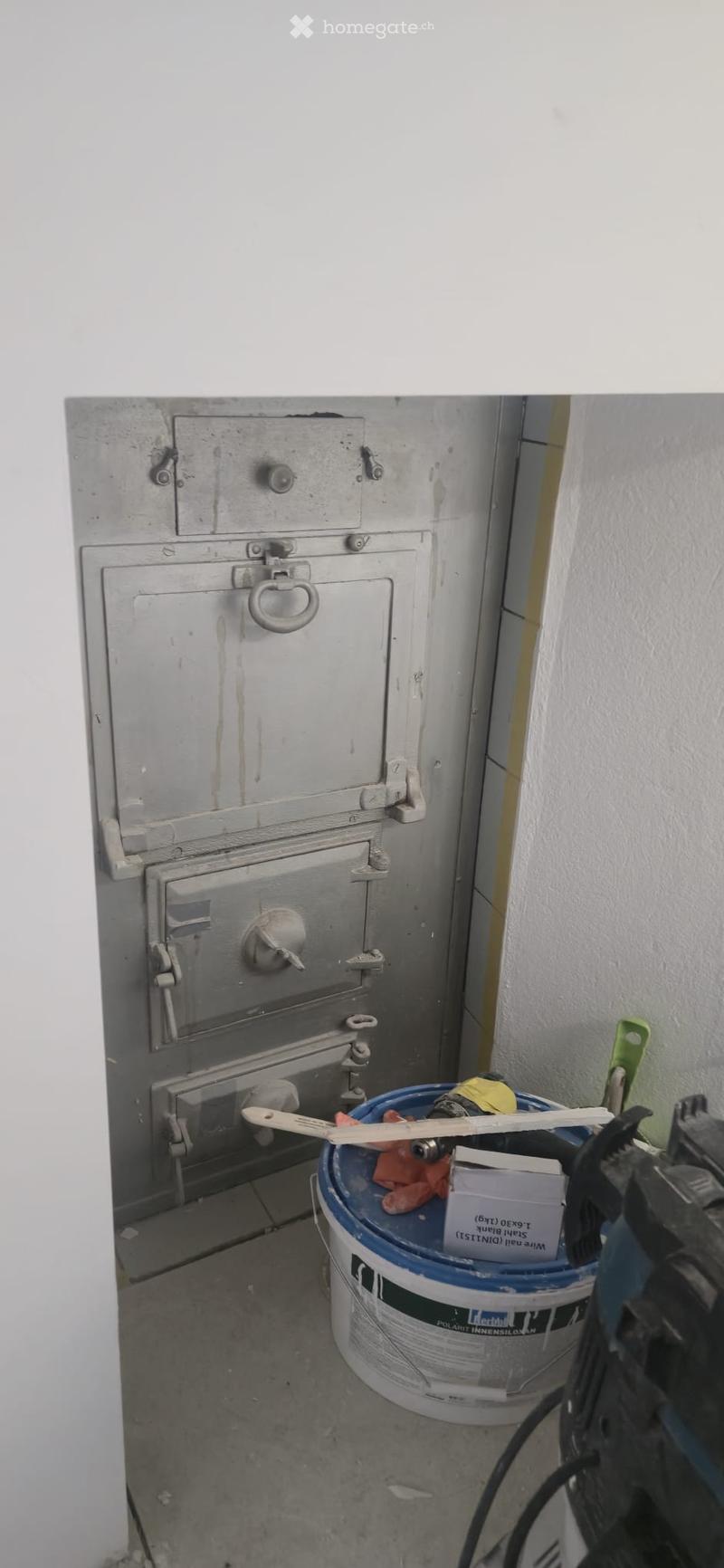 Empty utility room with a metal cabinet, a bucket with tools, and a partially visible drill on the floor.