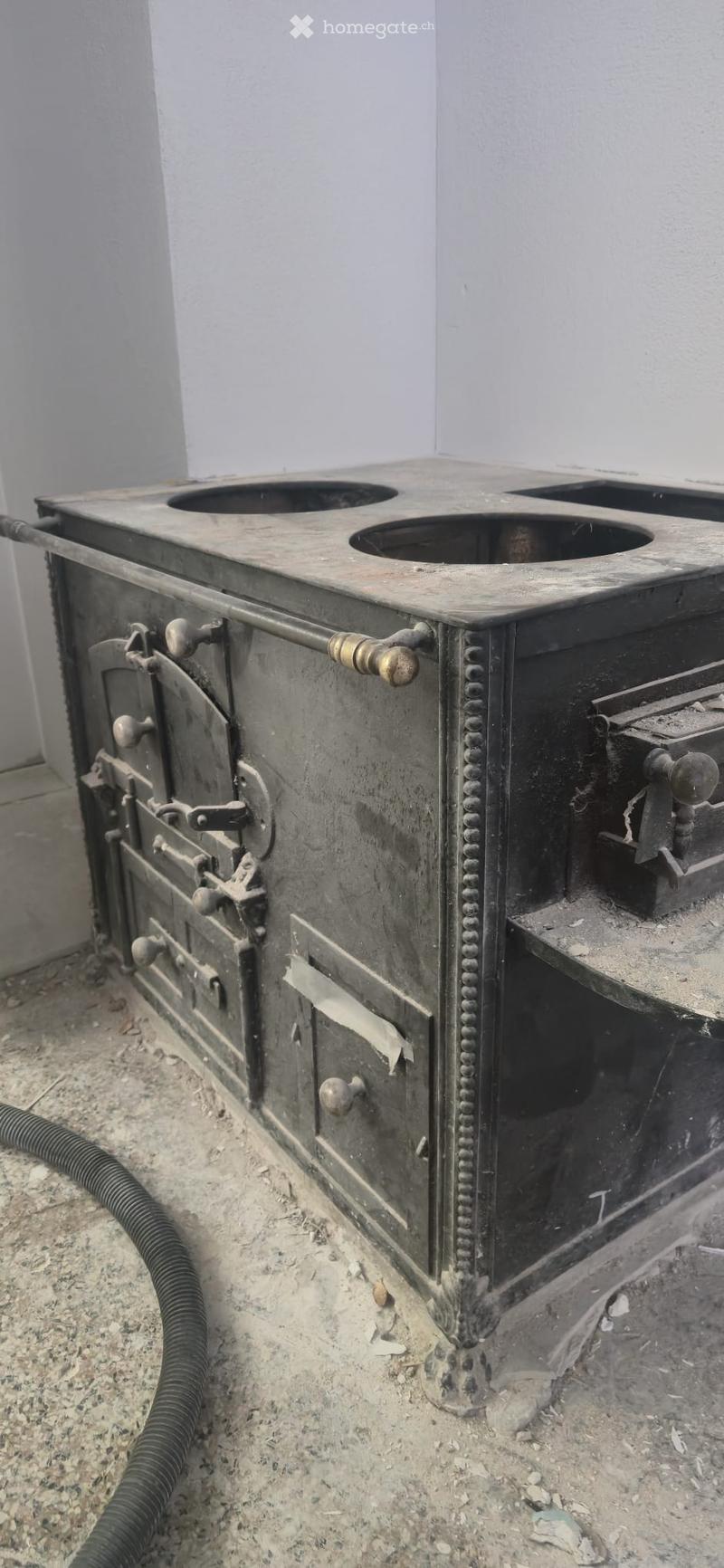 An old, rustic metal stove with multiple burners and intricate decorative handles, placed on a concrete floor.