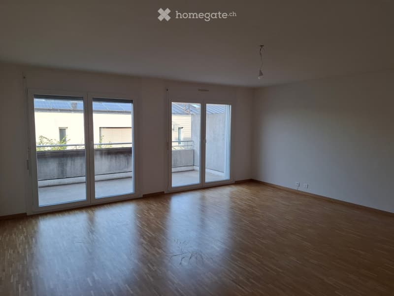 Empty room with wooden flooring, large sliding glass doors leading to a balcony, and white walls.
