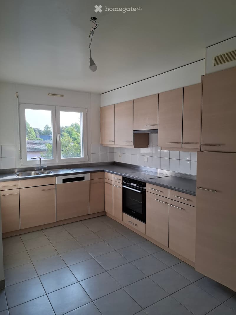 Modern kitchen with light wood cabinets, stainless steel appliances, tiled floor, and large windows.