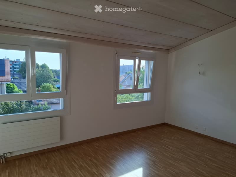 Empty room with wooden flooring, white walls, large windows, radiator, and visible electrical outlets.