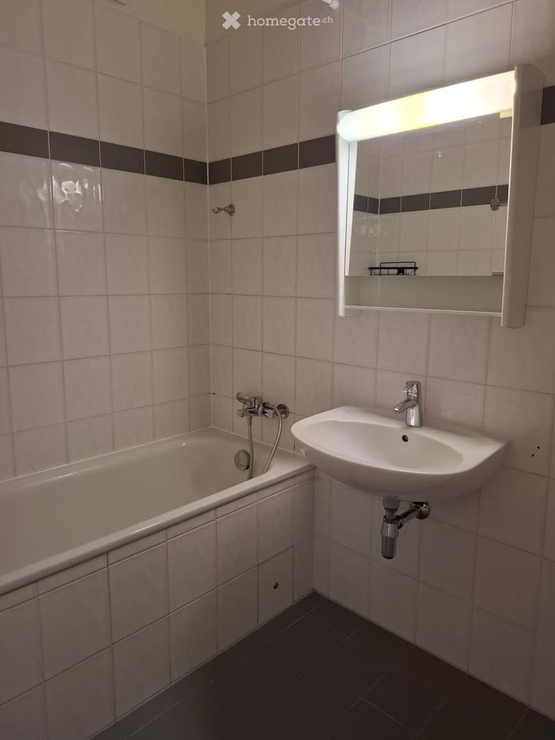 Bathroom with a bathtub, sink, mirror, and light fixture. The walls are tiled with a black and white border design.