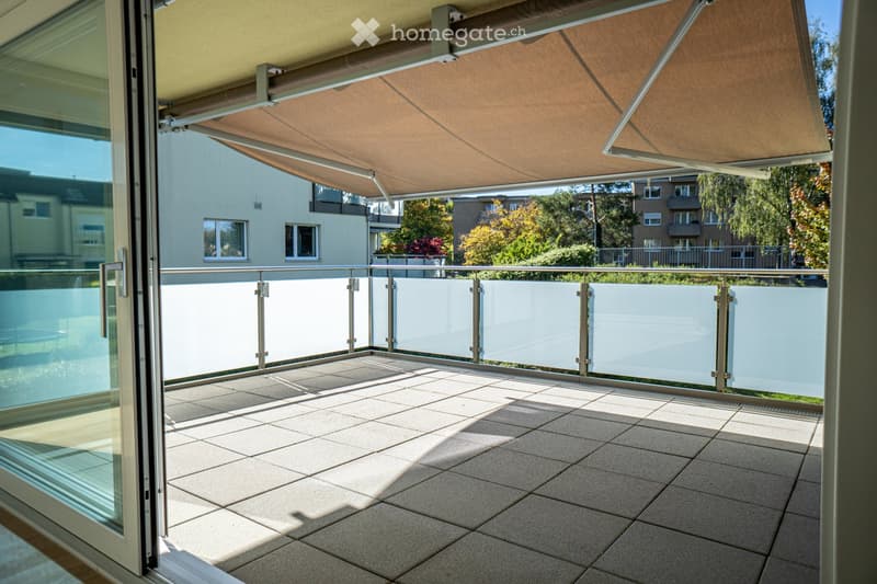 Balcony with tiled floor, glass railing, and retractable awning providing shade.