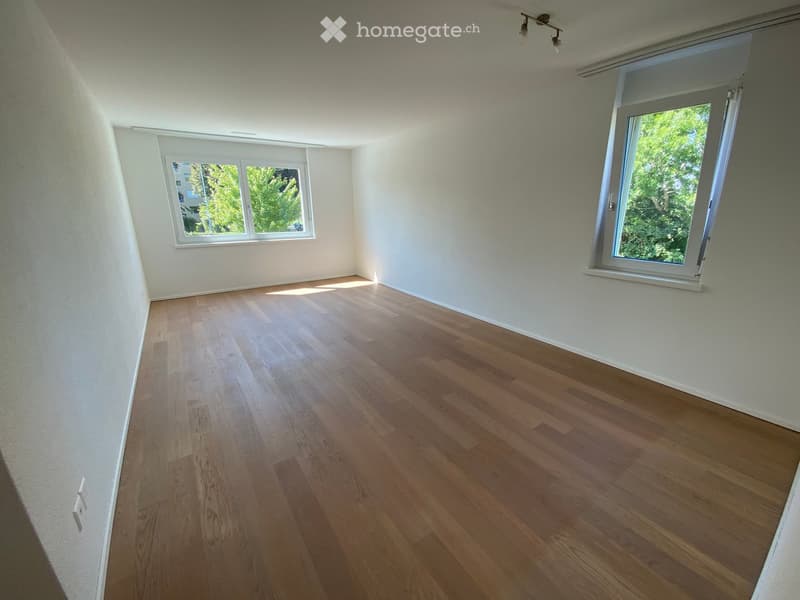 Empty room with wooden flooring and white walls, featuring two windows with white frames and a ceiling light fixture.
