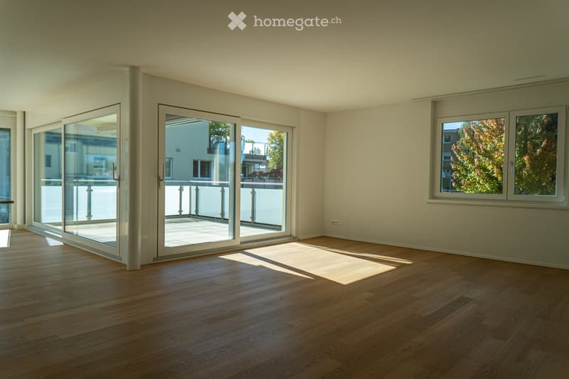 Empty room with wooden flooring, large sliding glass doors leading to a balcony, and a window with a view of trees.