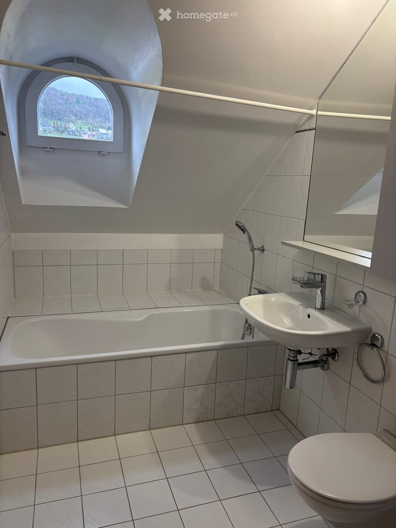 Modern bathroom with a bathtub, sink, toilet, and a large window offering a scenic view.