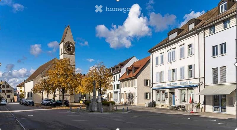 European town square with historic buildings, a church tower, and a few parked cars.