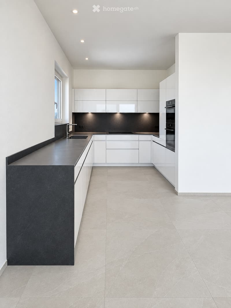 Modern kitchen with white cabinets, black countertops, and a built-in oven. The space features sleek, minimalist design with a large window and recessed lighting.