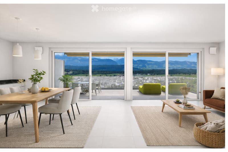 Open-plan living and dining area with large windows offering a scenic mountain view. Features a grey sofa, wooden coffee table, dining table with chairs, and decorative vases with plants.