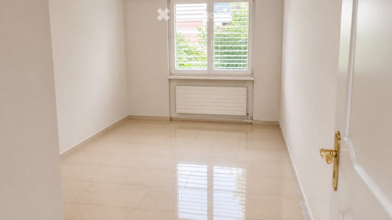 Empty room with tiled floor, white walls, a window with blinds, and a radiator below the window.