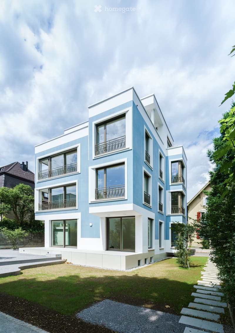 Modern two-story house with light blue and white exterior, large windows, and balconies.