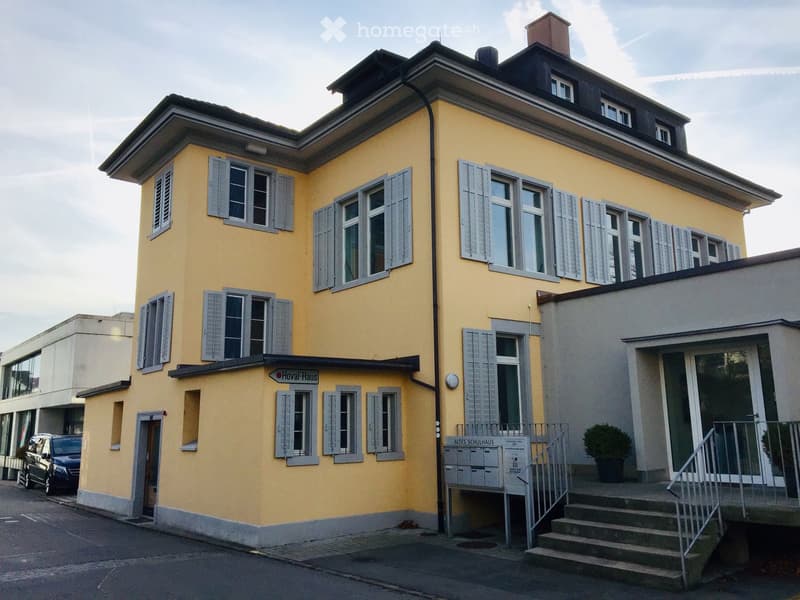 Three-story yellow building with gray shutters, multiple windows, and a sign reading 'Hoval-Haus'.