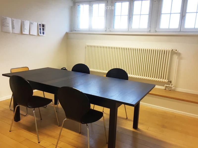 Meeting room with a large dark wooden table and several black chairs, natural light from windows, radiator, and wooden flooring.