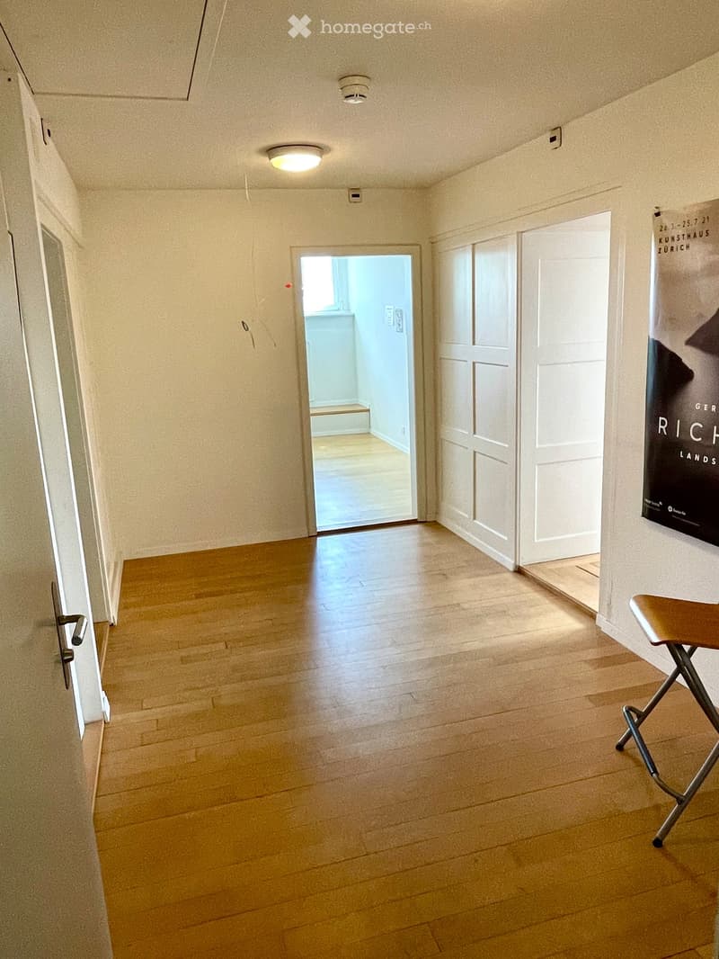 Empty hallway with wooden flooring, white walls, and several doors leading to other rooms.