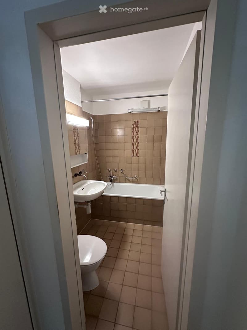 Small bathroom with beige tiles, a toilet, a sink, and a bathtub, viewed from an open doorway.
