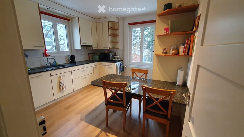 Bright kitchen with white cabinets, granite countertop, sink, microwave, and a small dining area with a table and chairs.