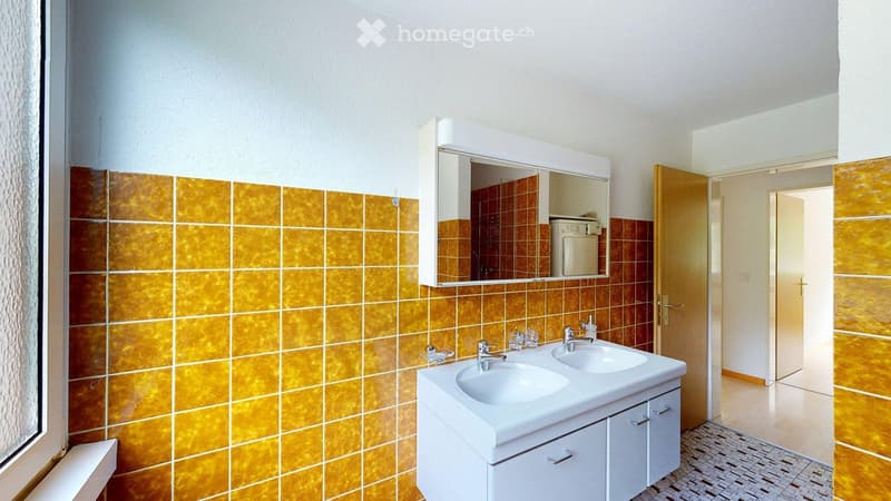 Bathroom with double sink, mirror cabinet, and tiled walls in orange and brown.