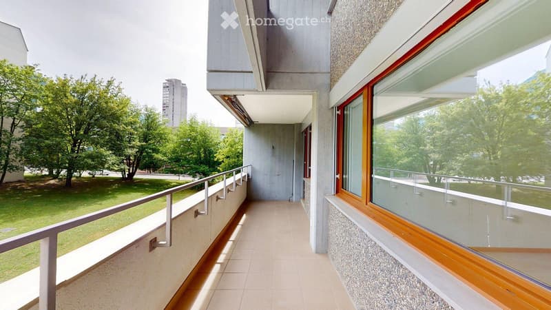 Balcony with tiled floor, metal railing, large windows, and a view of a green lawn and trees.