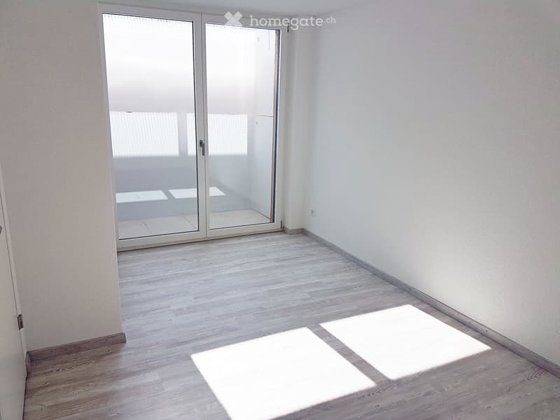 Empty room with light wooden flooring, white walls, and a large sliding glass door leading to an outdoor area.