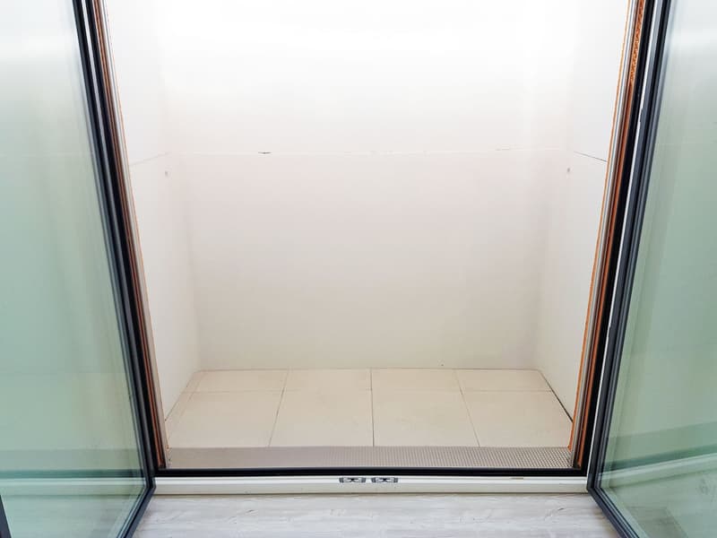 Empty room with light-colored tiled floor and white walls, featuring a large glass sliding door with a textured glass panel.