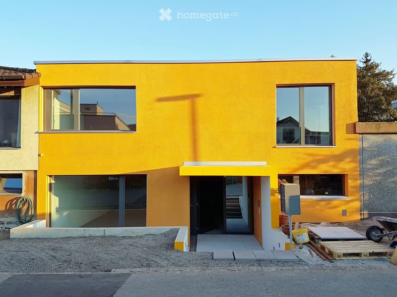 Modern residential building, yellow exterior walls, large windows, entrance with canopy, under construction