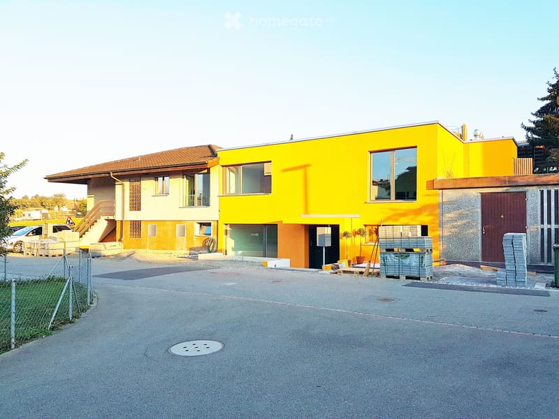 Modern apartment building with yellow and brown exterior, large windows, and a rooftop terrace.