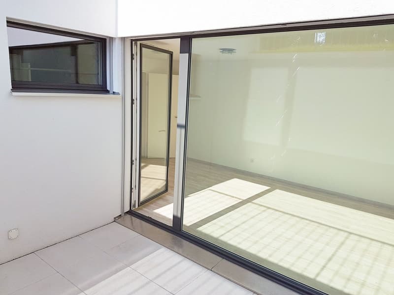 Modern balcony with large glass sliding doors, tiled floor, and white walls.