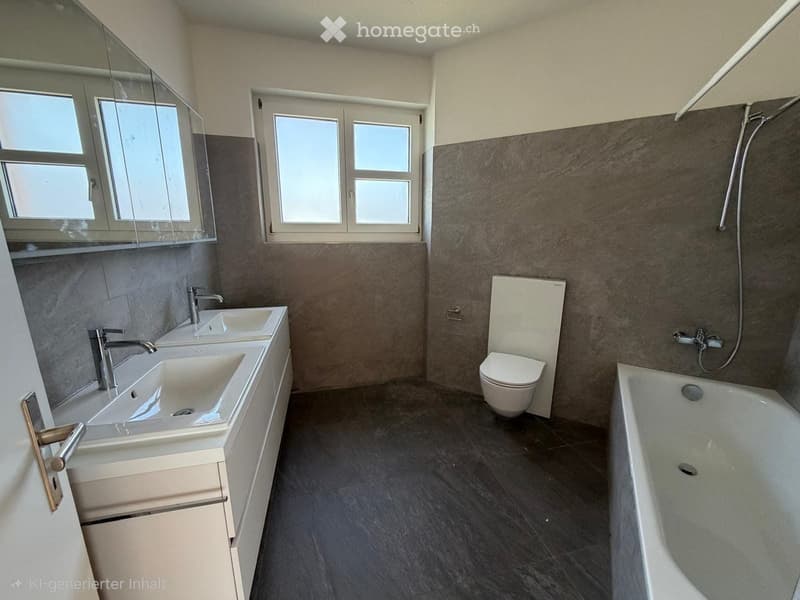 Modern bathroom with double sink, bathtub, toilet, and large mirror. Dark tiled walls and floor, natural light from windows.
