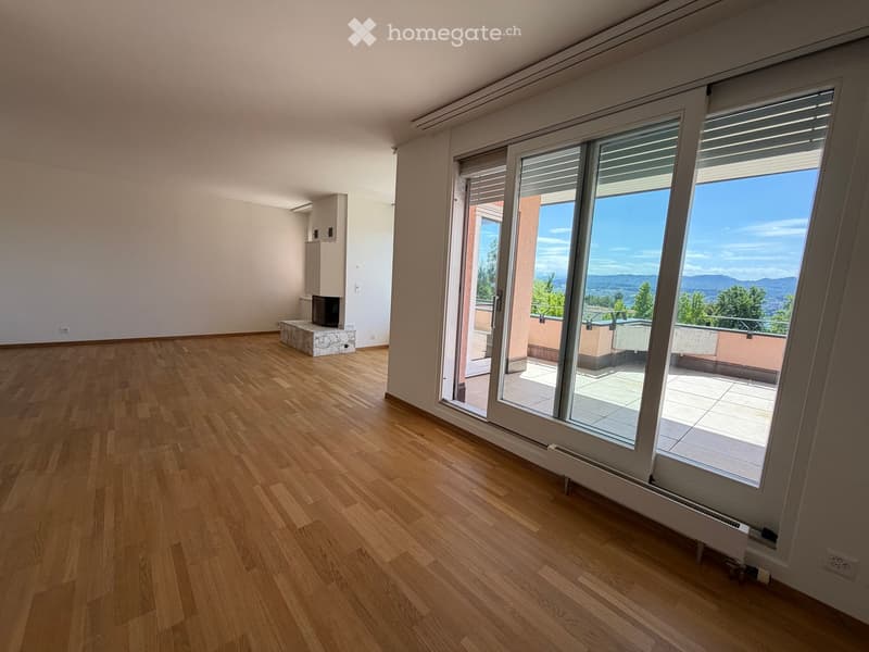 Empty room with wooden flooring, large sliding glass doors leading to a balcony, and a small fireplace on the left side.